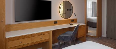 Una habitación de hotel moderna con una cama grande, un escritorio de madera, un televisor de pantalla plana, un espejo redondo y un vestidor.
