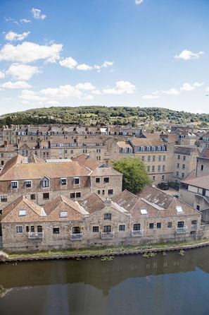 A historic stone building with multiple windows and balconies, situated by a calm river.