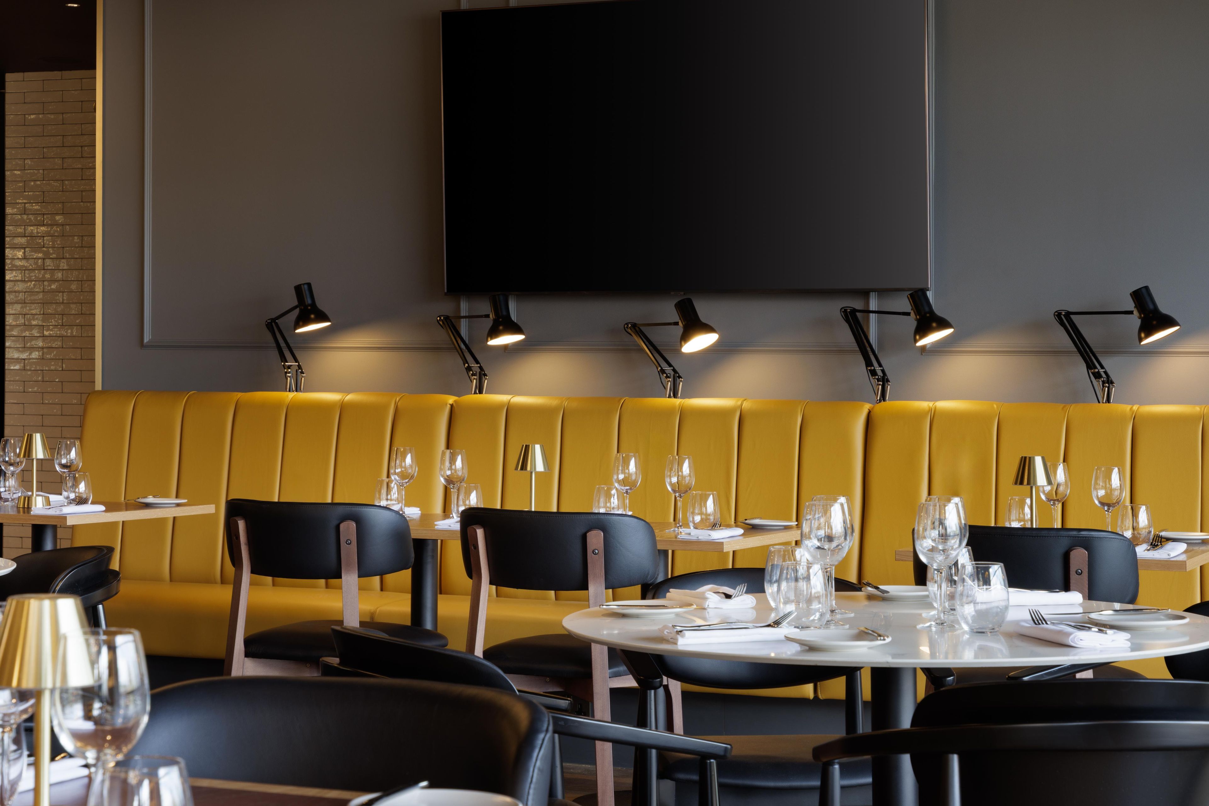 L’intérieur d’un restaurant avec des banquettes jaunes, des tables rondes et des chaises noires.
