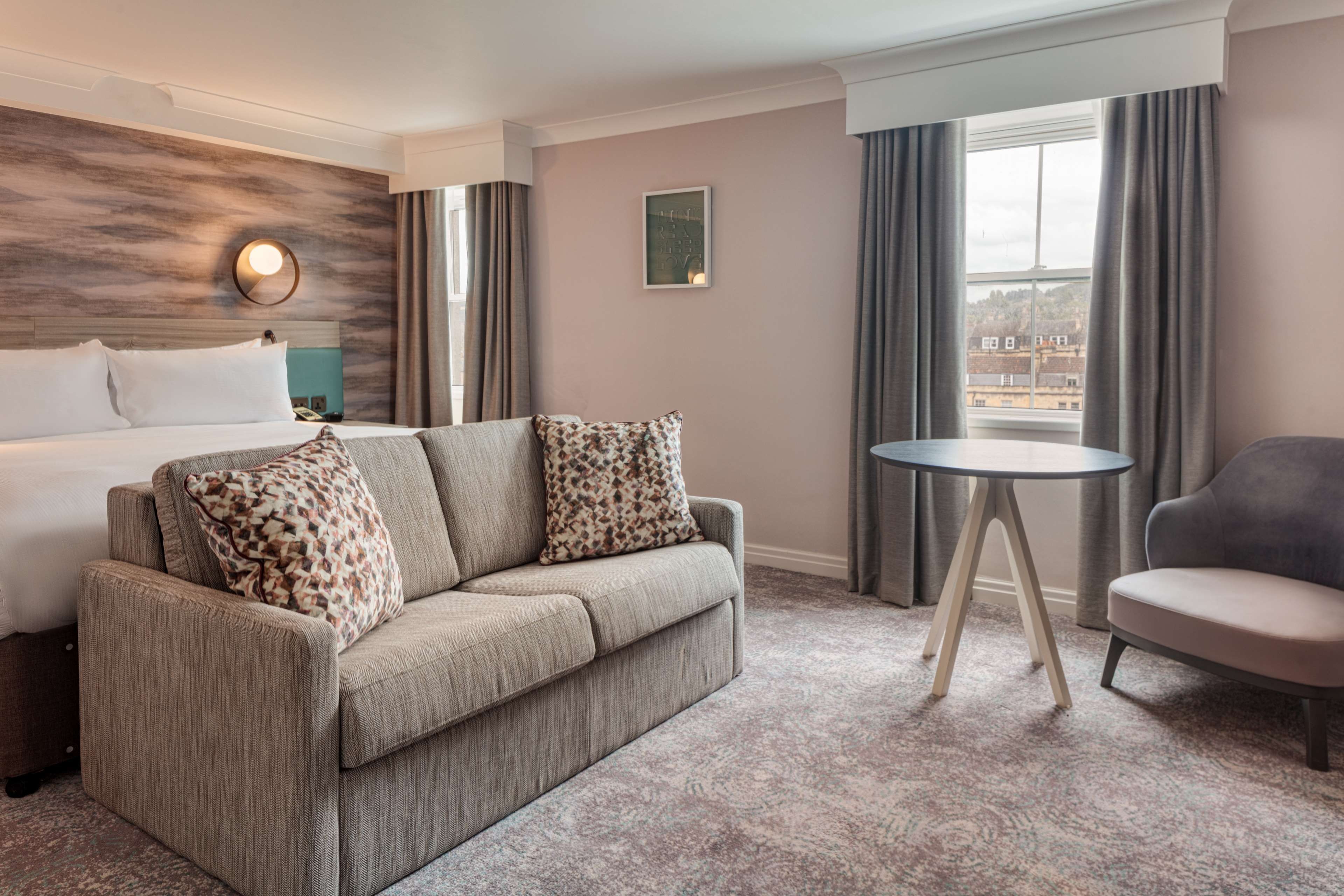 Habitación de hotel con cama, sofá, una silla, una mesita y vistas al exterior.