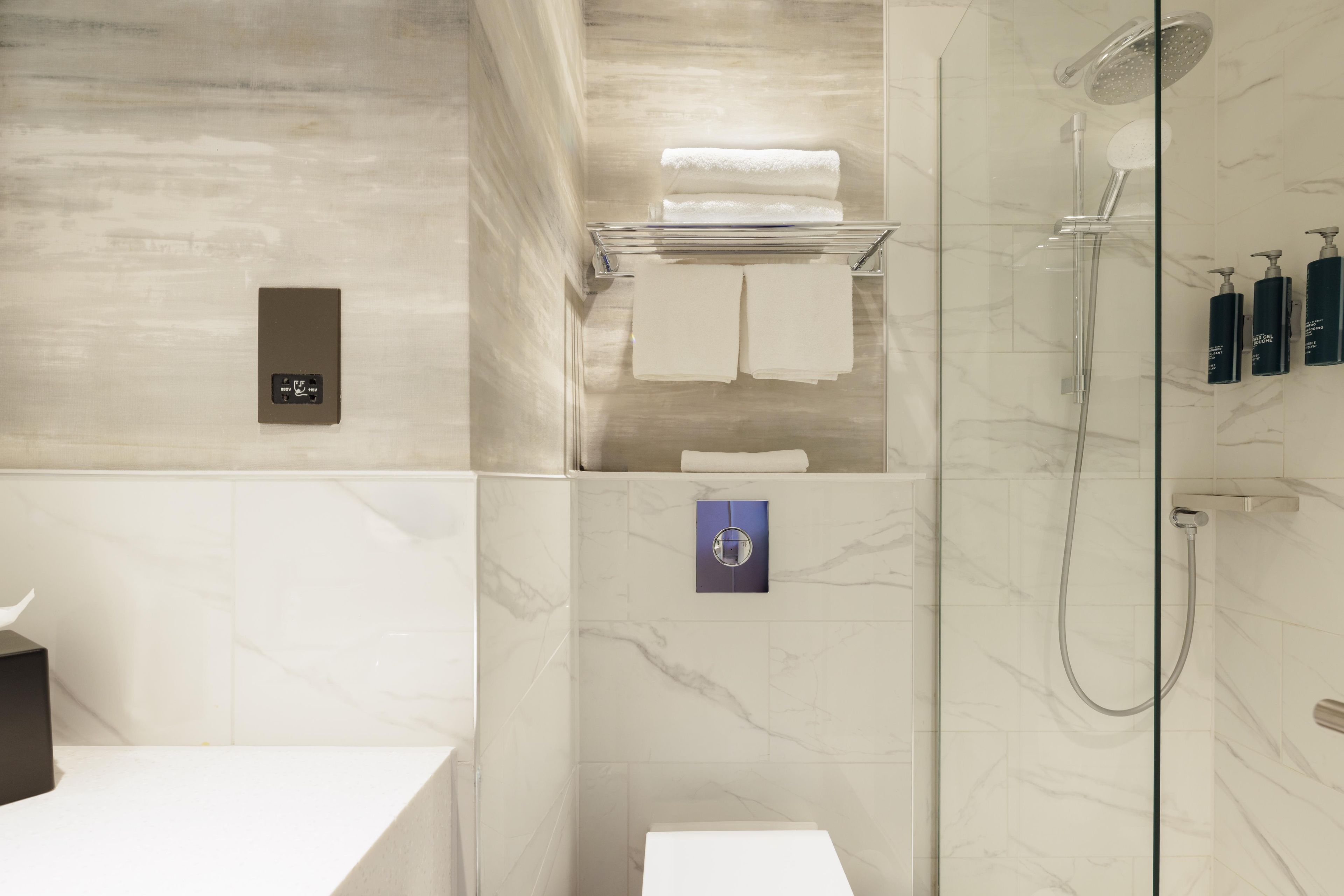 A modern bathroom with a glass shower enclosure, a white sink, and a towel rack with folded towels.
