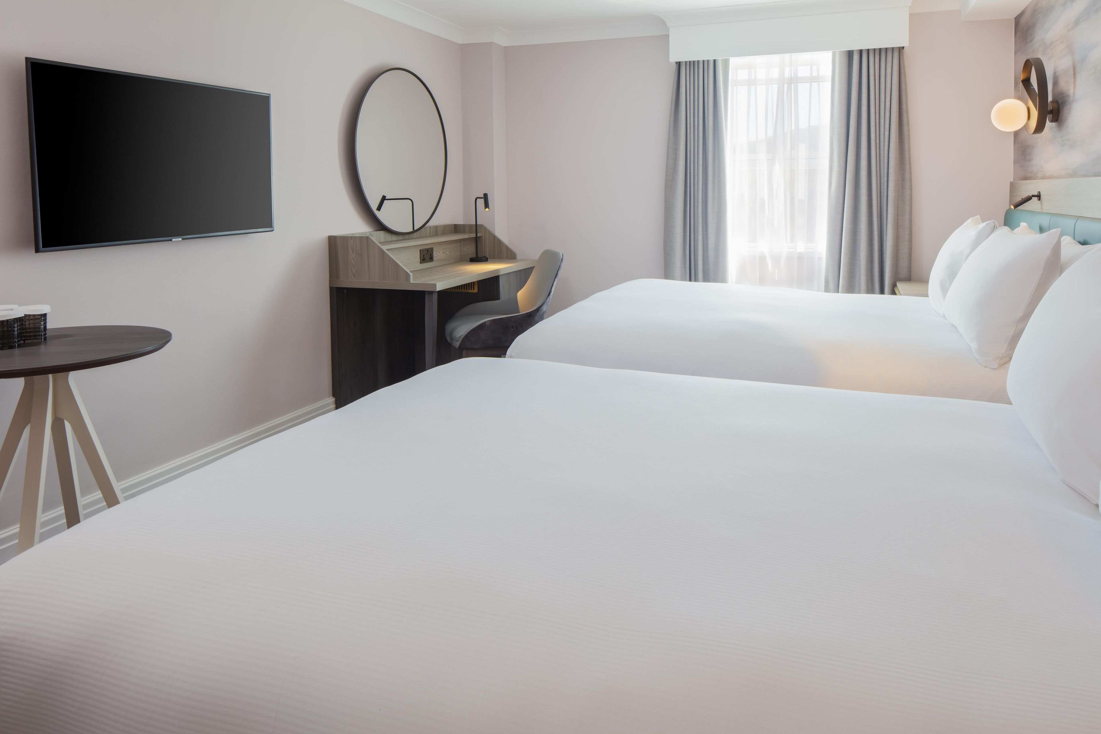 A hotel room with a large bed, a desk, a chair, a TV, and a window with curtains.