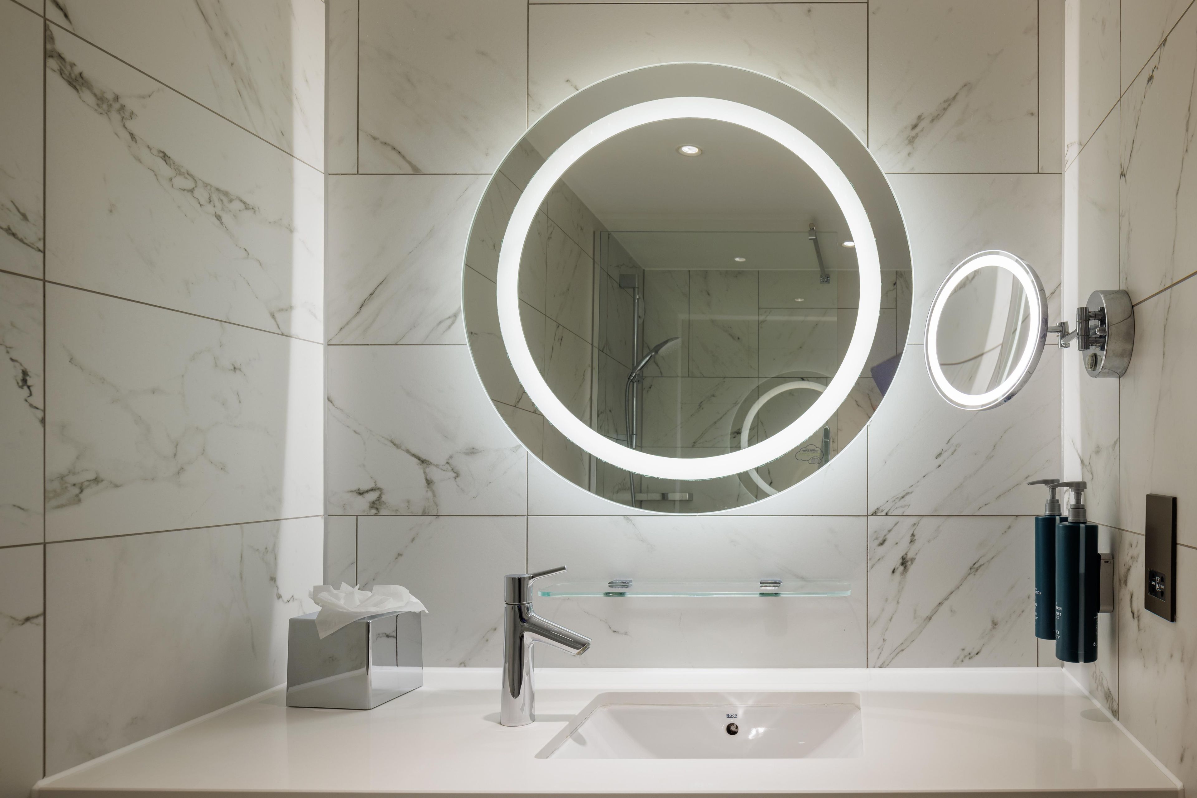 A modern bathroom with a large mirror, a sink, and a shower.