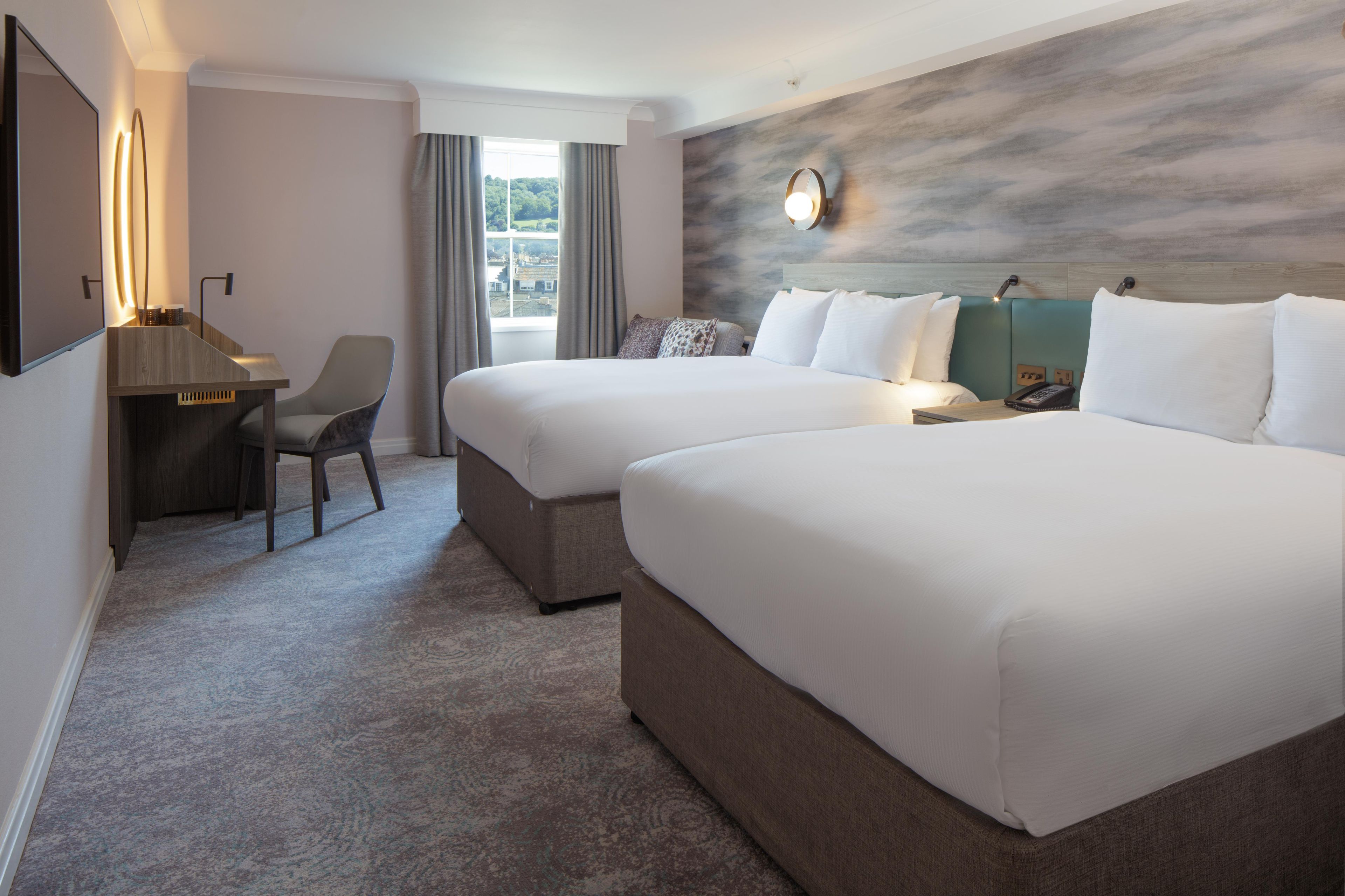 A hotel room with two beds, a desk, and a chair.
