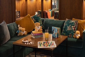 A cozy living room with a green sofa, a coffee table with books, a teddy bear, and a board game.