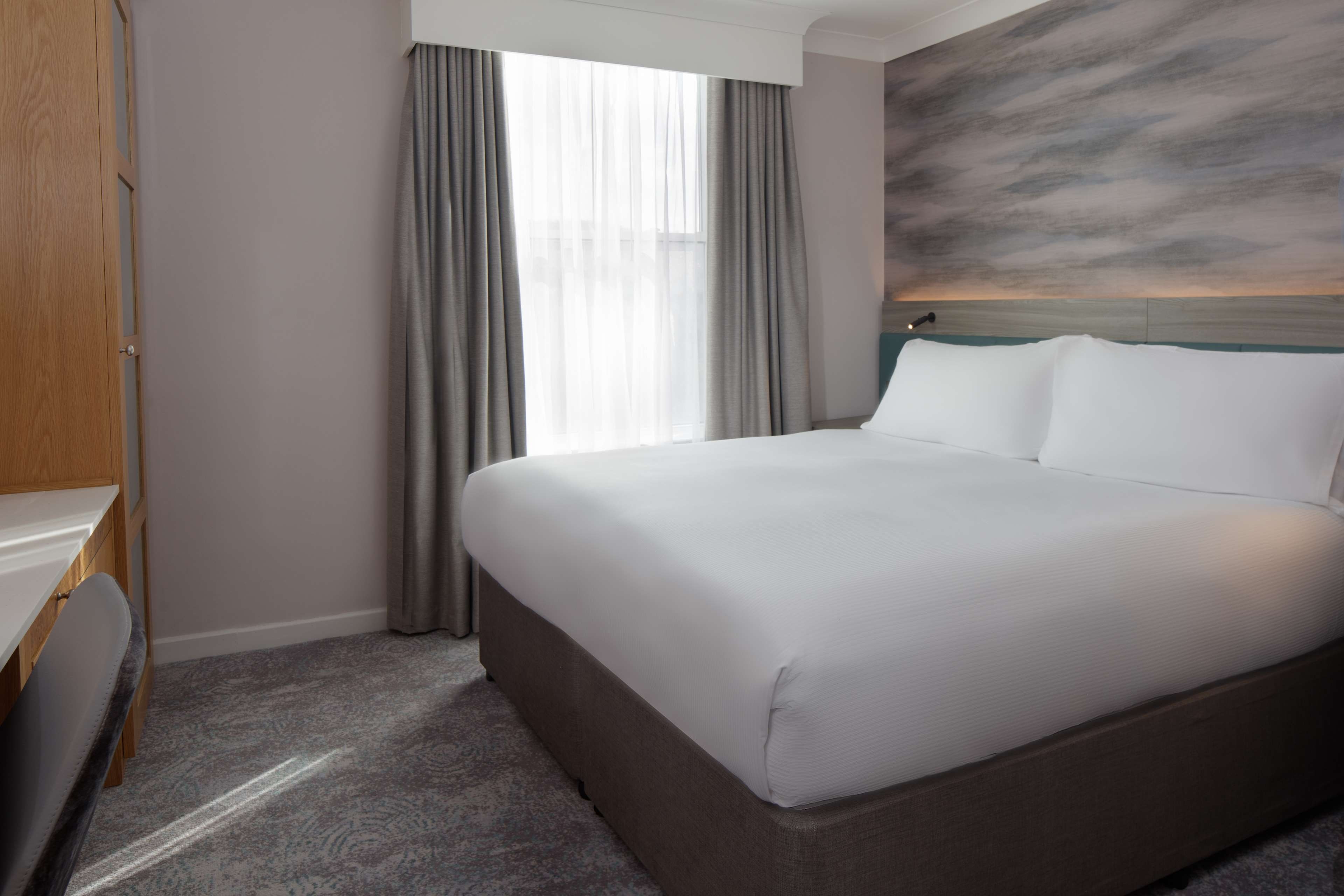 Habitació d'hotel amb un llit gran, un escriptori i vista al cel per la finestra.