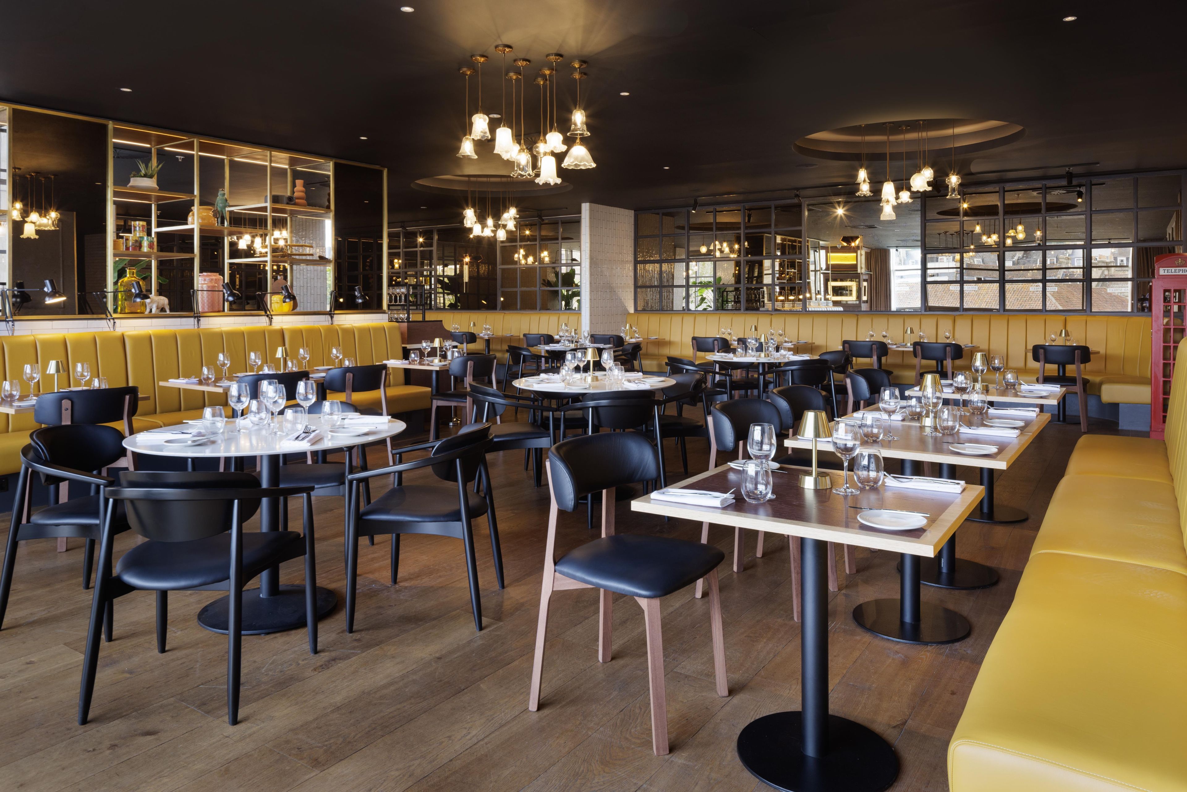 L'intérieur d'un restaurant avec des tables rondes, des chaises noires et des banquettes jaunes.