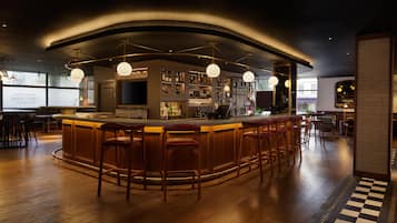 Una zona de bar con un mostrador curvo, varios taburetes y una variedad de botellas y vasos.
