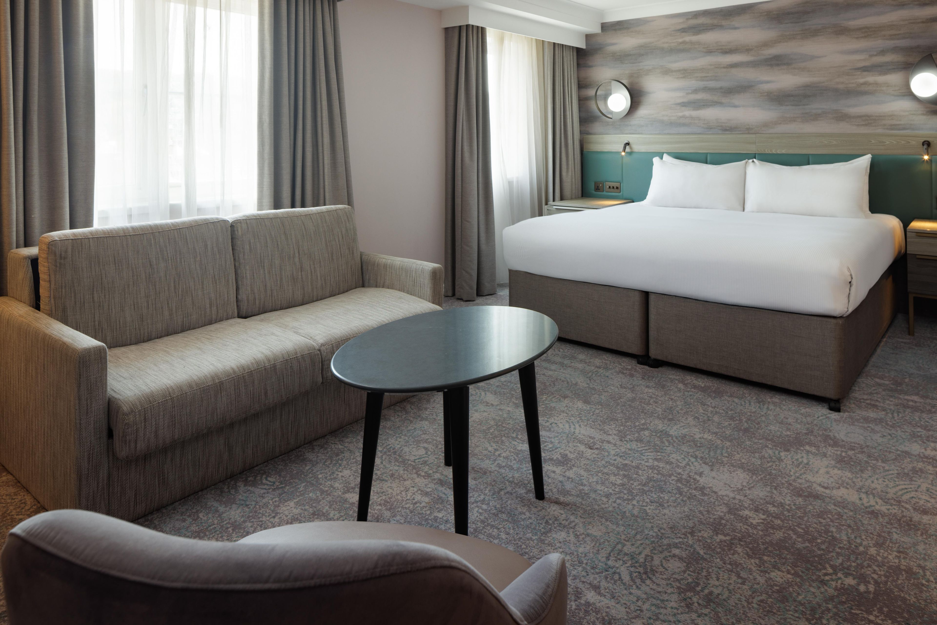 A hotel room with a sofa, a bed, a small table, and a nightstand.