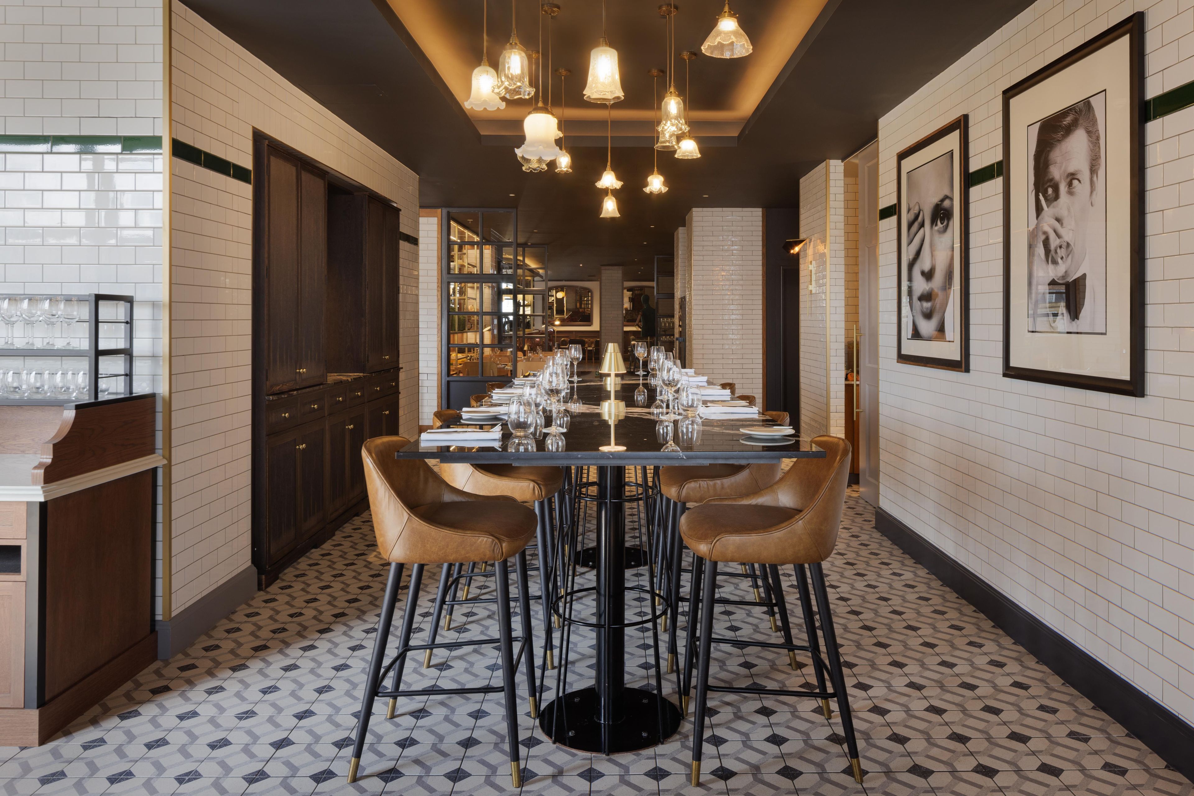 Un restaurant avec une longue table dressée pour le dîner, des tabourets de bar et des luminaires suspendus.