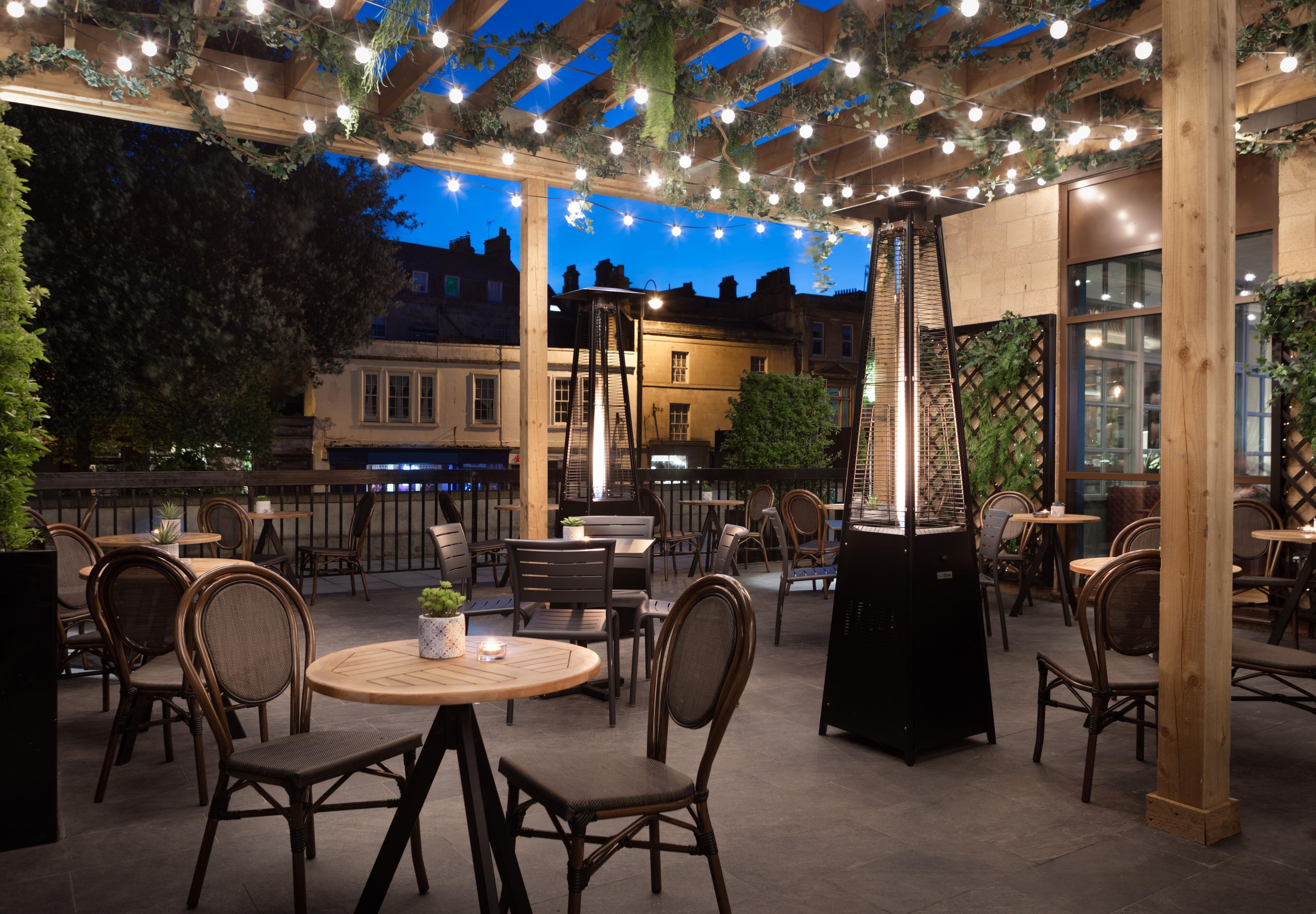 An outdoor patio with round tables and chairs, string lights, and a central heating unit.