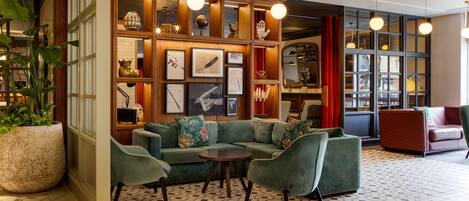 A lobby with a green sofa set, a large potted plant, and a wall with framed artwork.