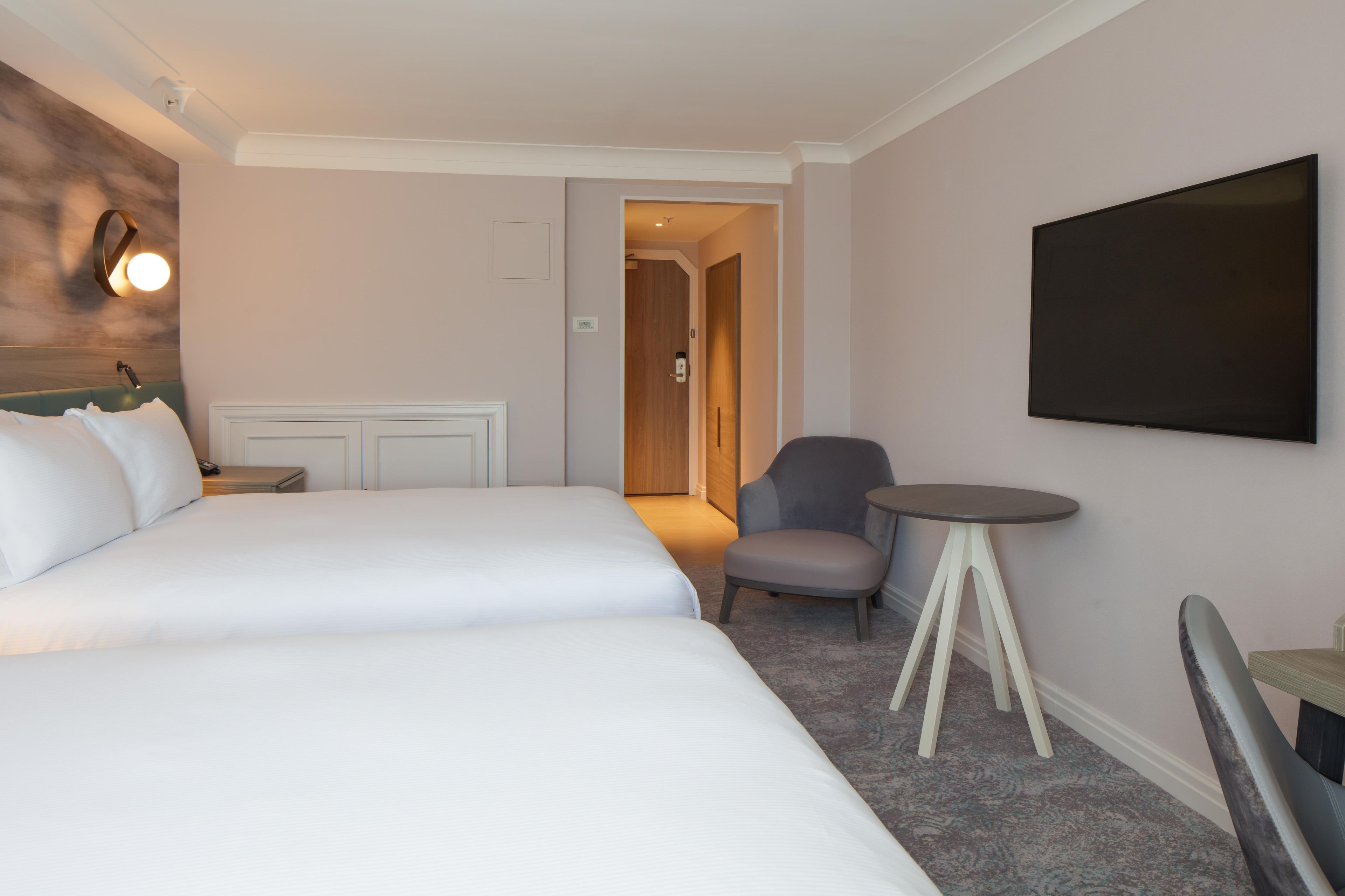 Una habitación de hotel con una cama, una silla, una mesita y un televisor en la pared.