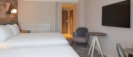 Una habitación de hotel con una cama, una silla, una mesita y un televisor en la pared.