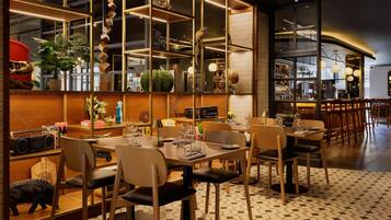 A restaurant with a modern interior, featuring a bar area with a mirrored wall, wooden furniture, and a variety of decorative items.