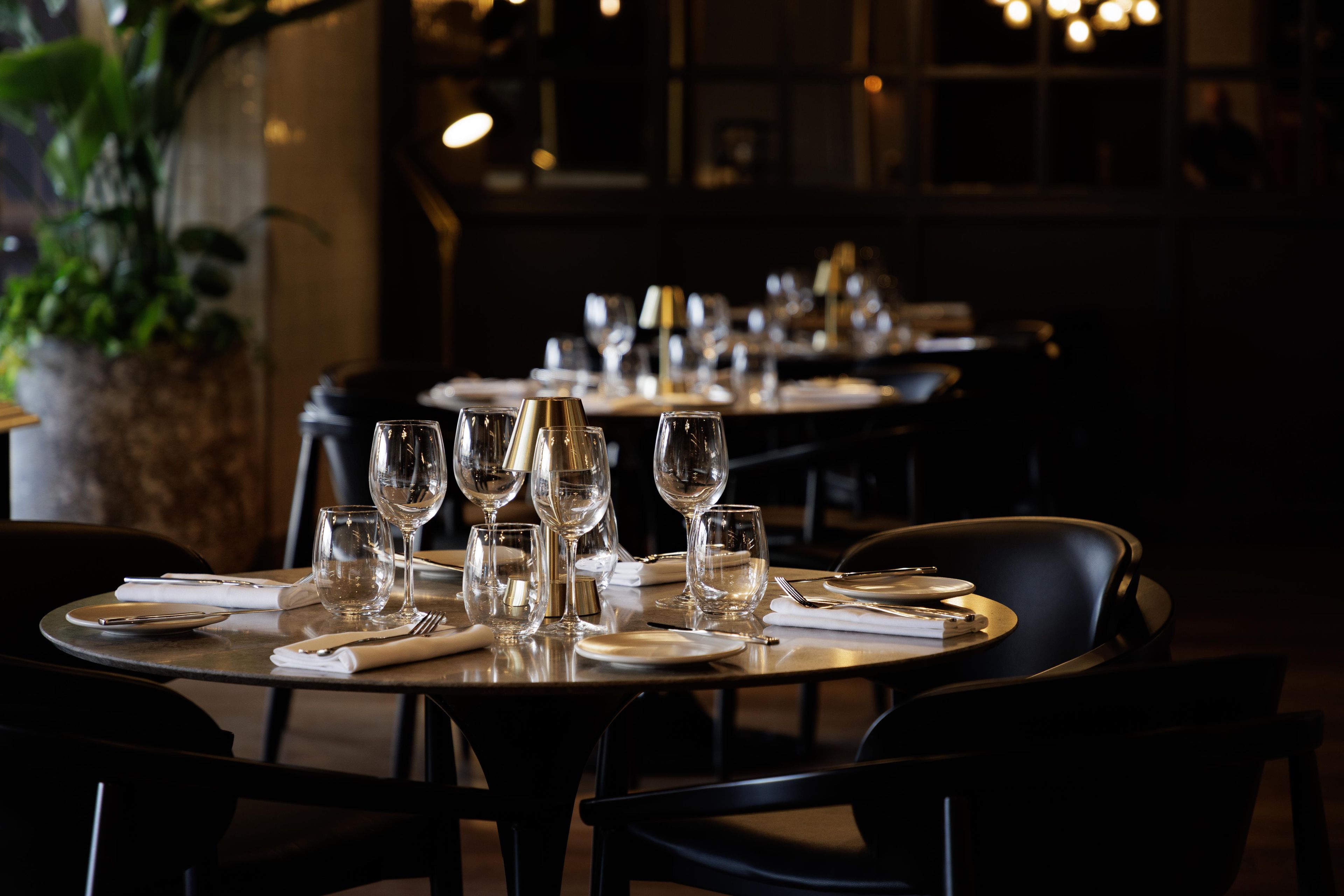 A restaurant interior with tables set for dining, featuring clear glassware and plates.