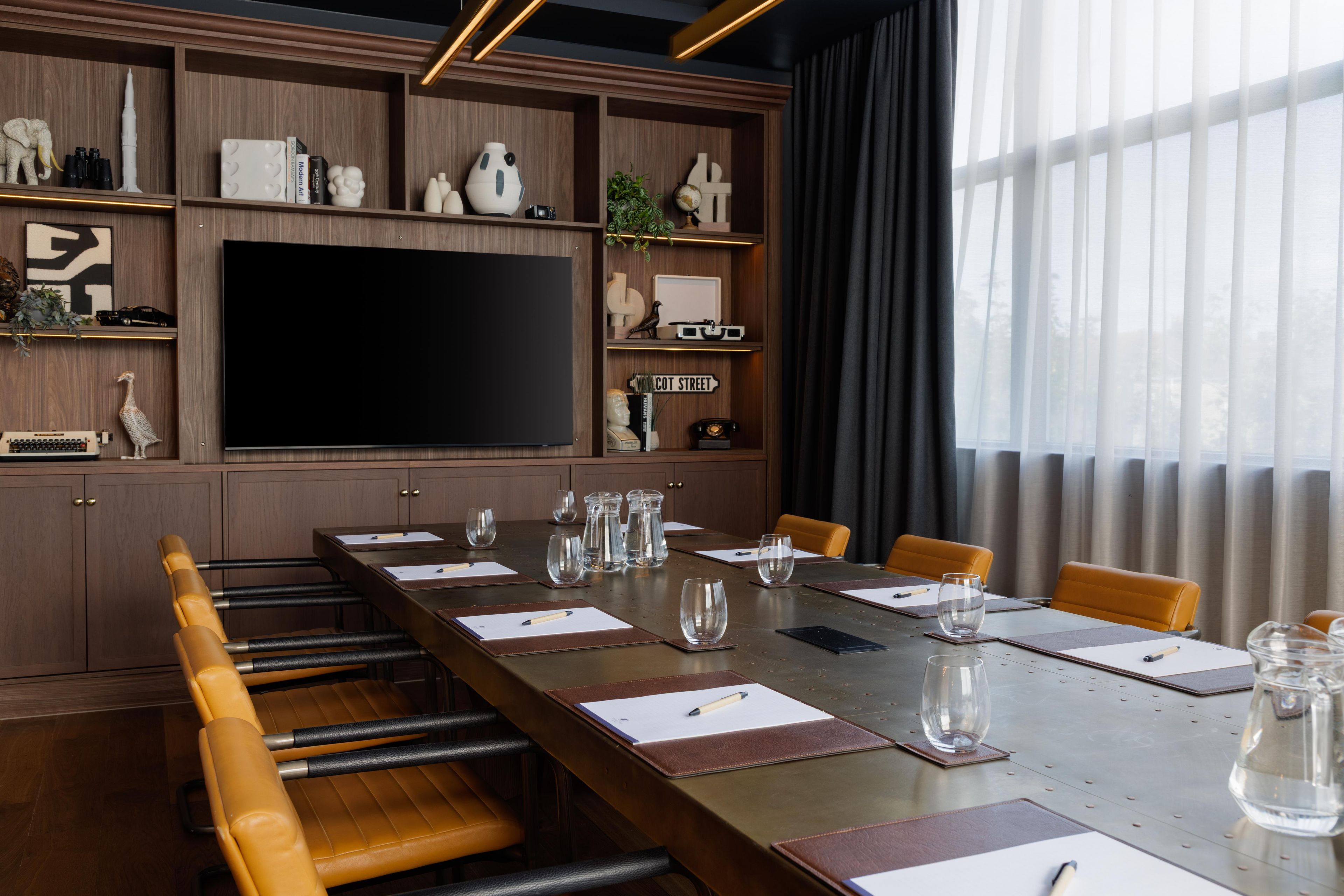 Une salle de conférence avec une longue table, des chaises, un grand téléviseur à écran plat et divers objets décoratifs disposés sur des étagères.