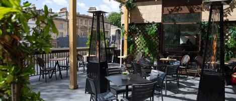 An outdoor patio with tables and chairs, surrounded by greenery and a pergola.