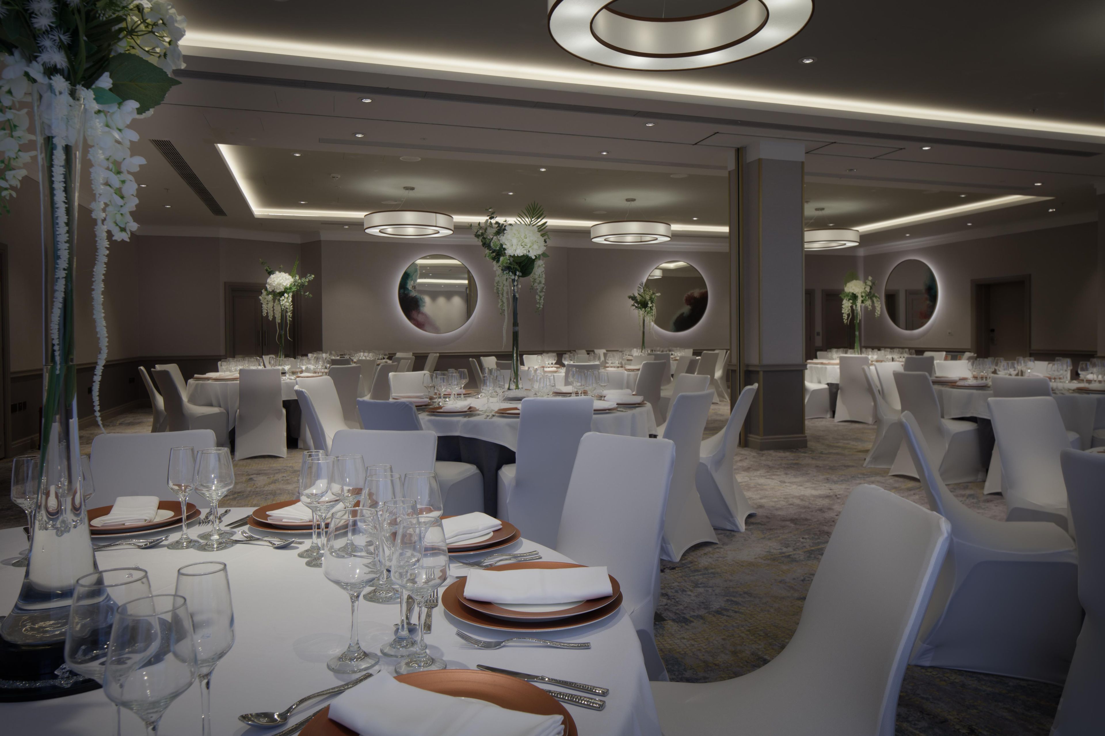 A banquet hall with round tables, white chairs, and elegant table settings.