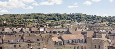 A historic town with traditional stone buildings, a dense arrangement of rooftops, and a backdrop of a forested hill.