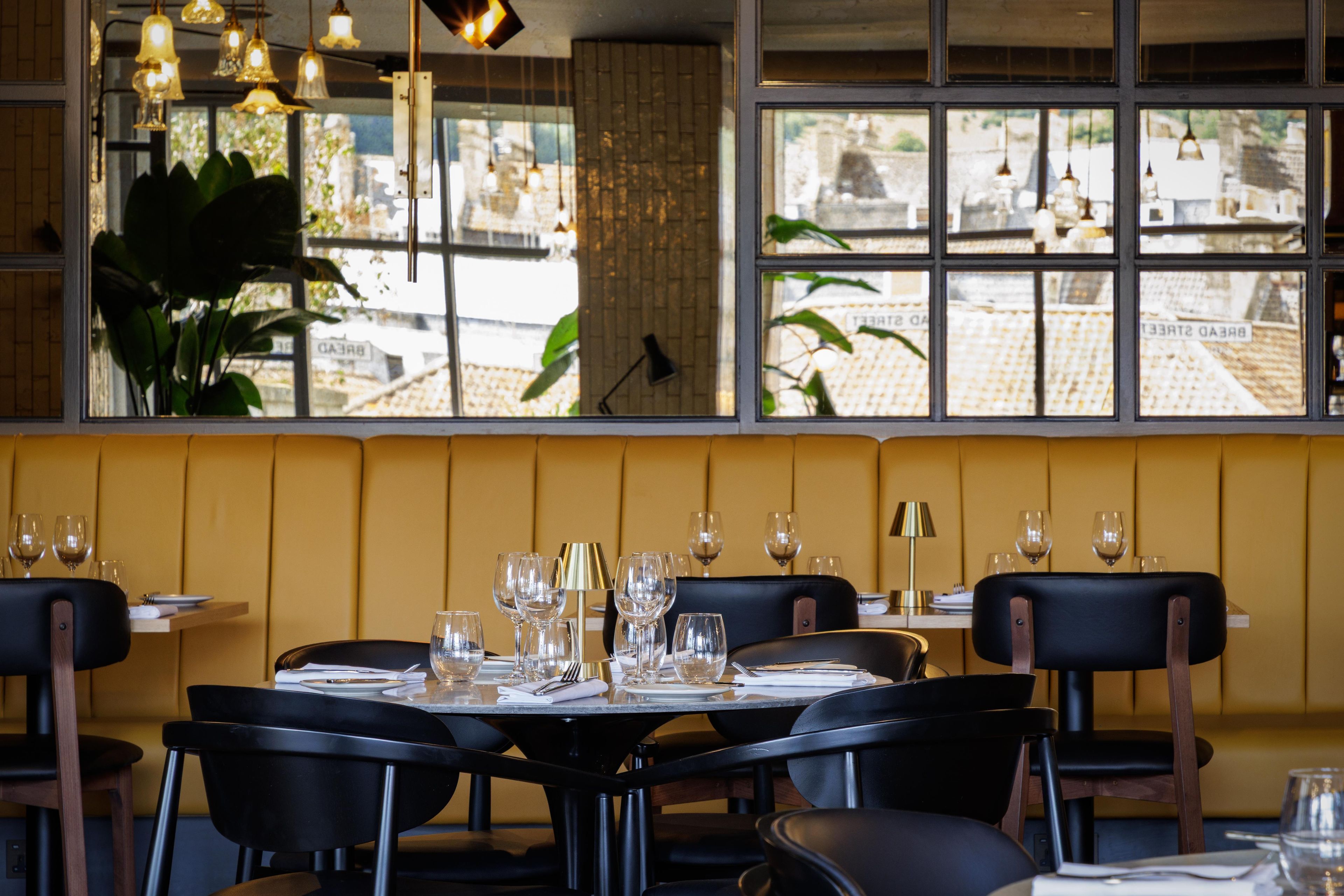 A restaurant interior with a table set for dining, chairs, and a view through the window.