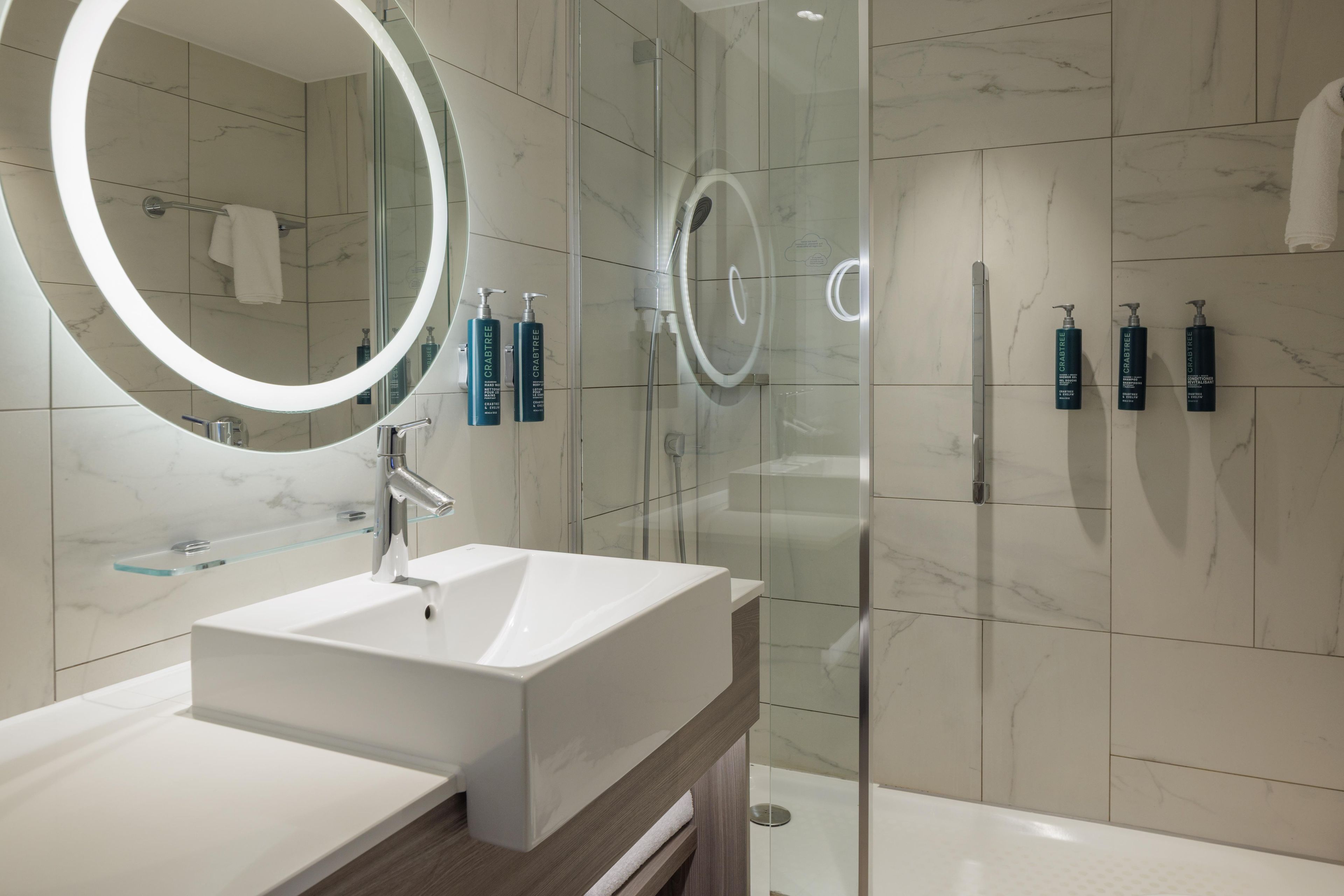 Une salle de bain moderne avec une douche à parois de verre, un lavabo blanc avec un miroir et des articles de toilette fixés au mur.