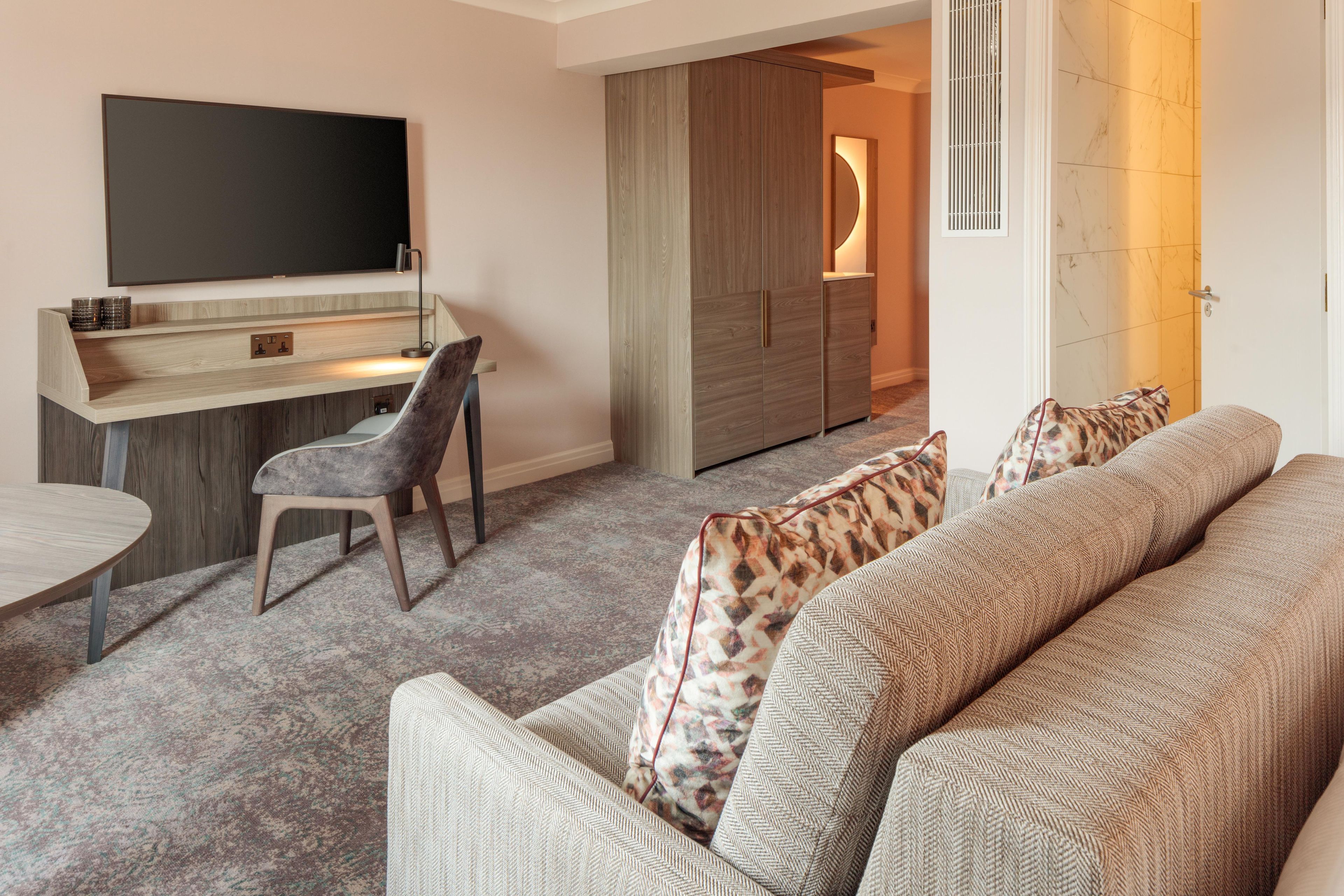 Een moderne woonkamer met een bank, een eettafel, een aan de muur bevestigde televisie en een inbouwkeuken.