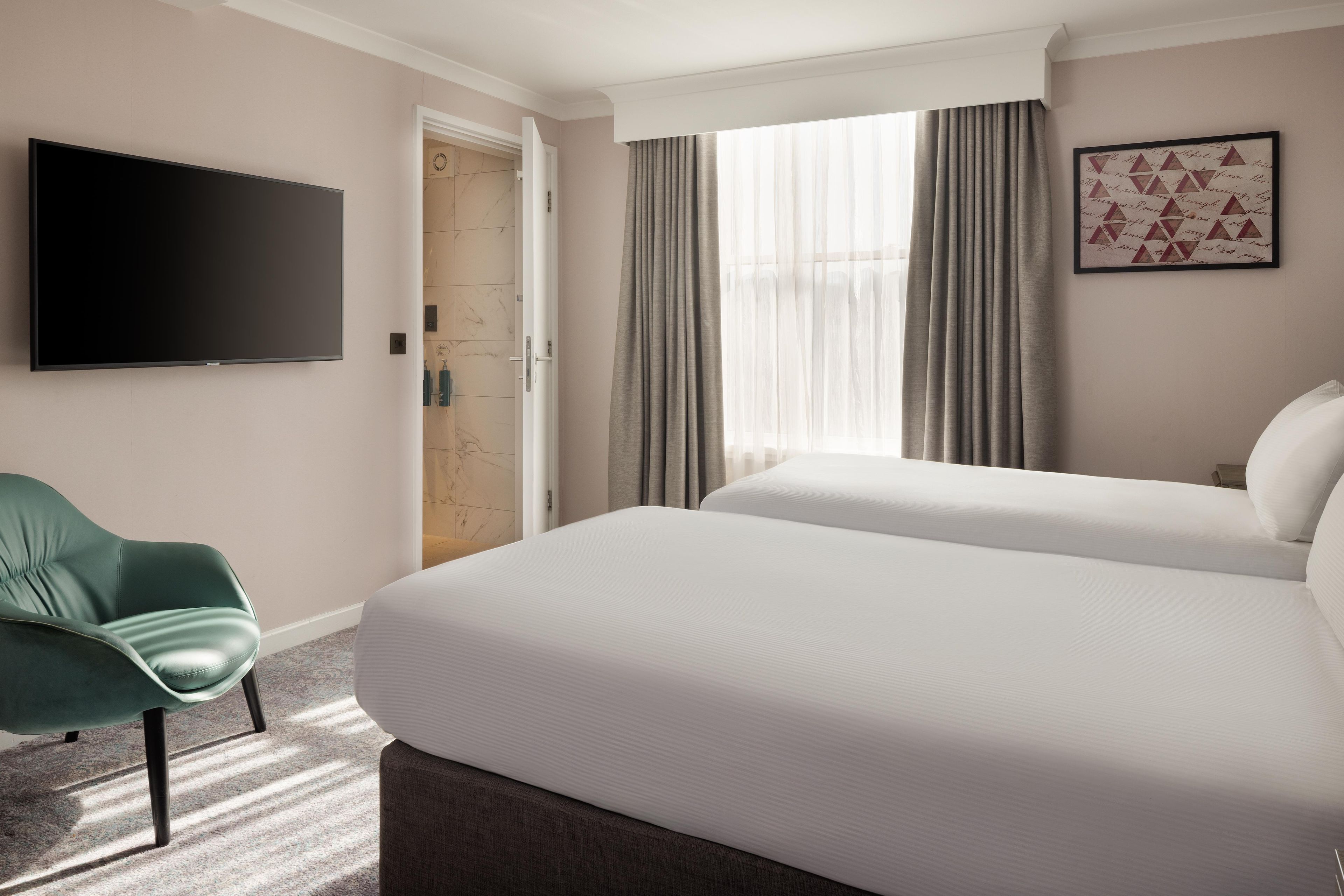 Une chambre d’hôtel avec un lit, une télévision, un fauteuil vert et un espace douche.
