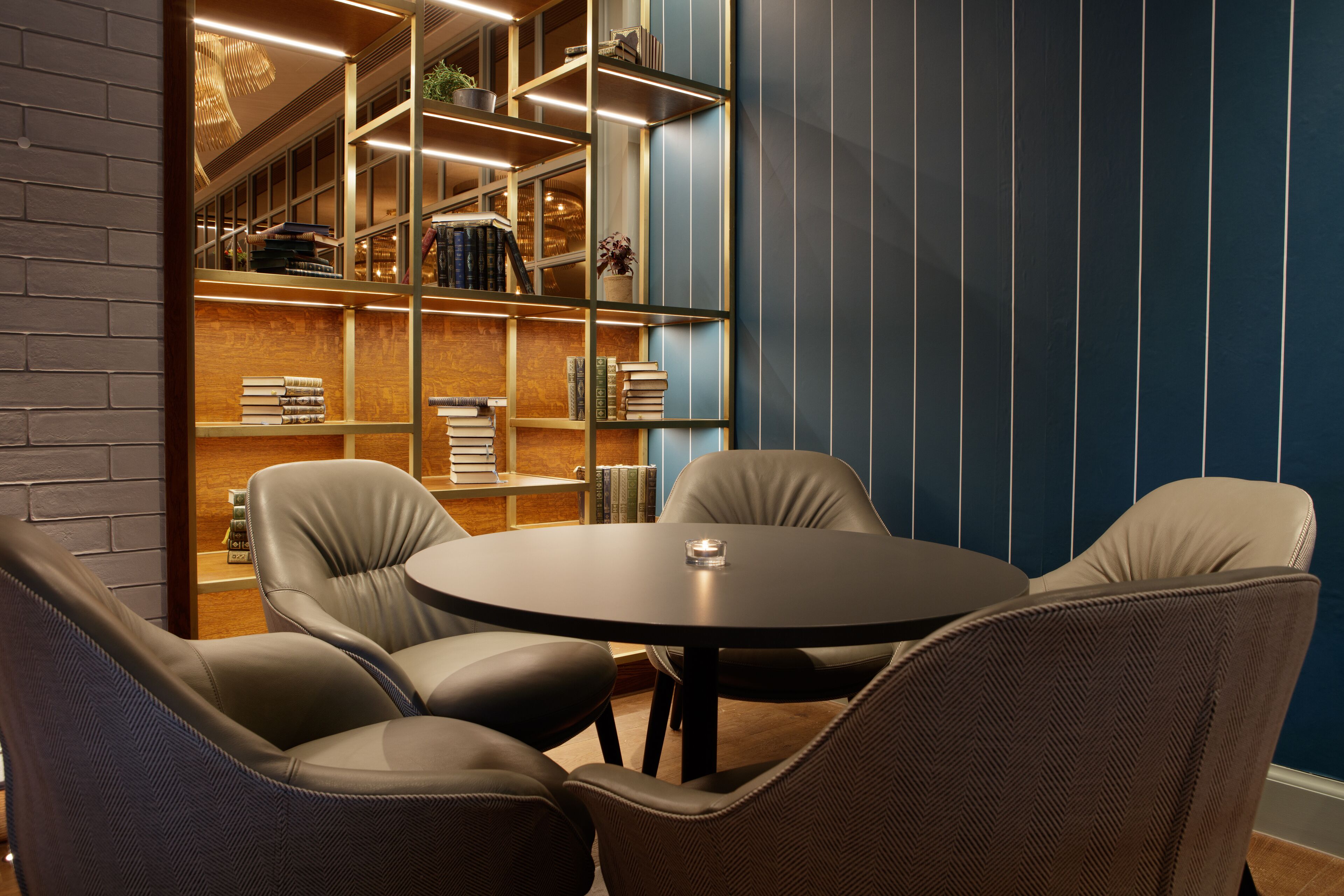 A modern library with a round table and leather chairs, surrounded by bookshelves.
