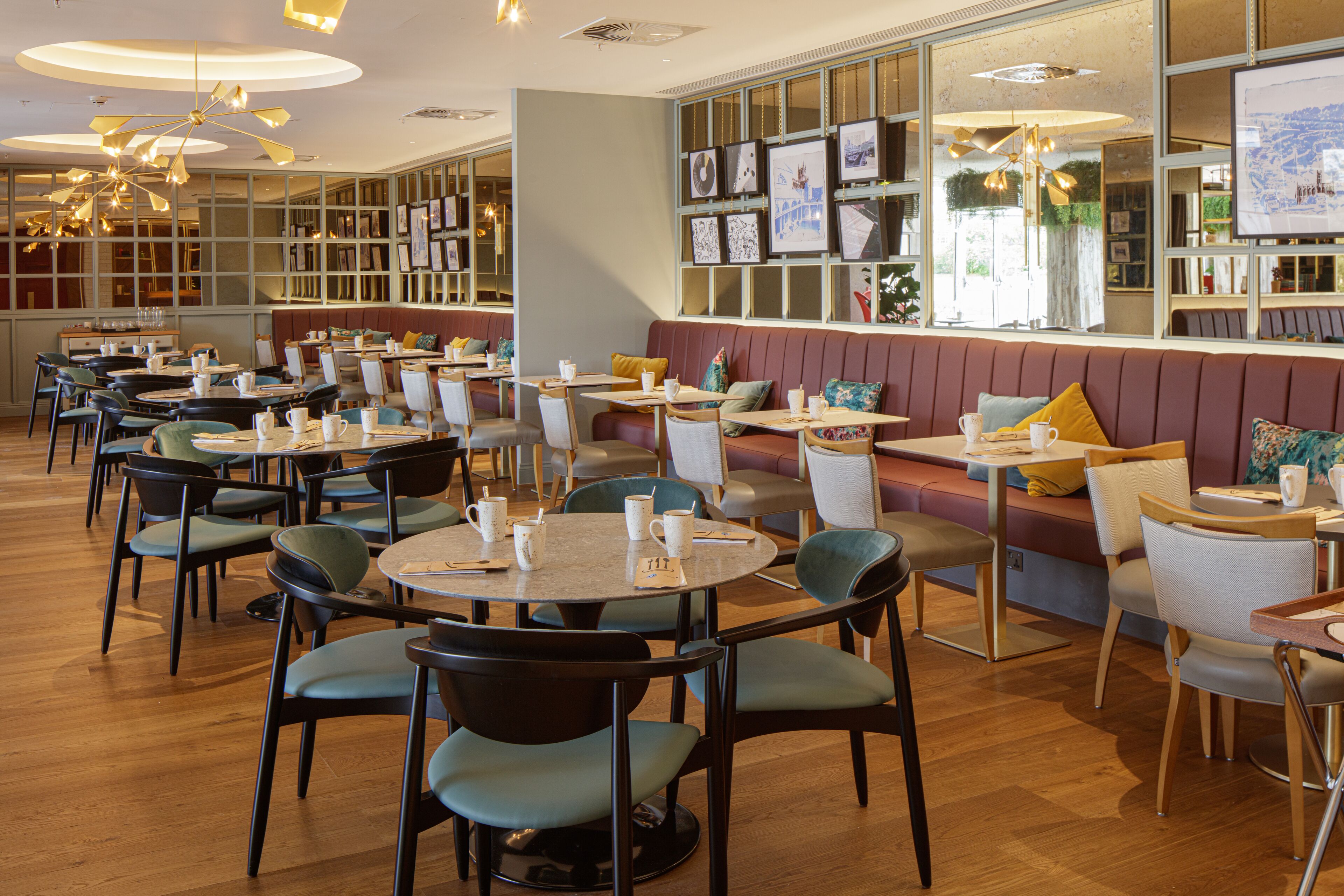 Een ruim restaurant met diverse zithoeken, waaronder perken en tafels, en een groot raam met kunstwerken.