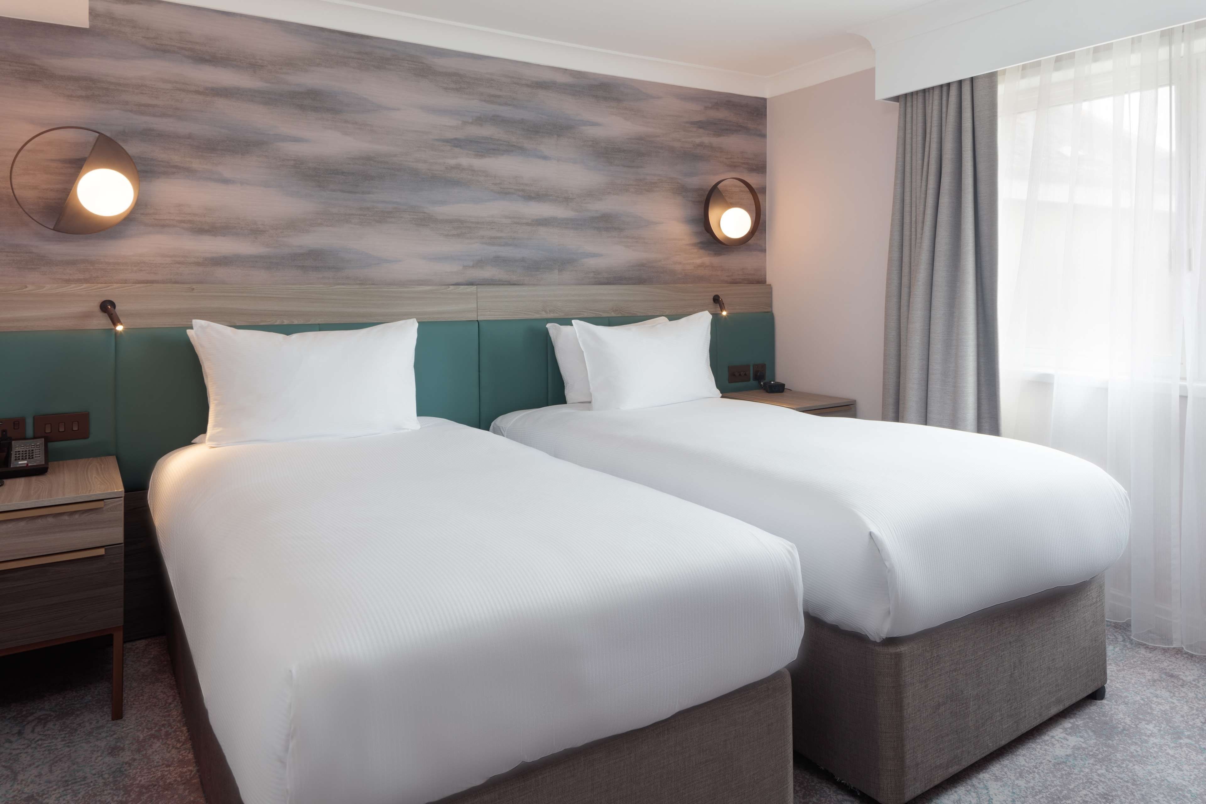 Une chambre d’hôtel avec deux lits, une tête de lit en bois et une table de chevet avec un téléphone.