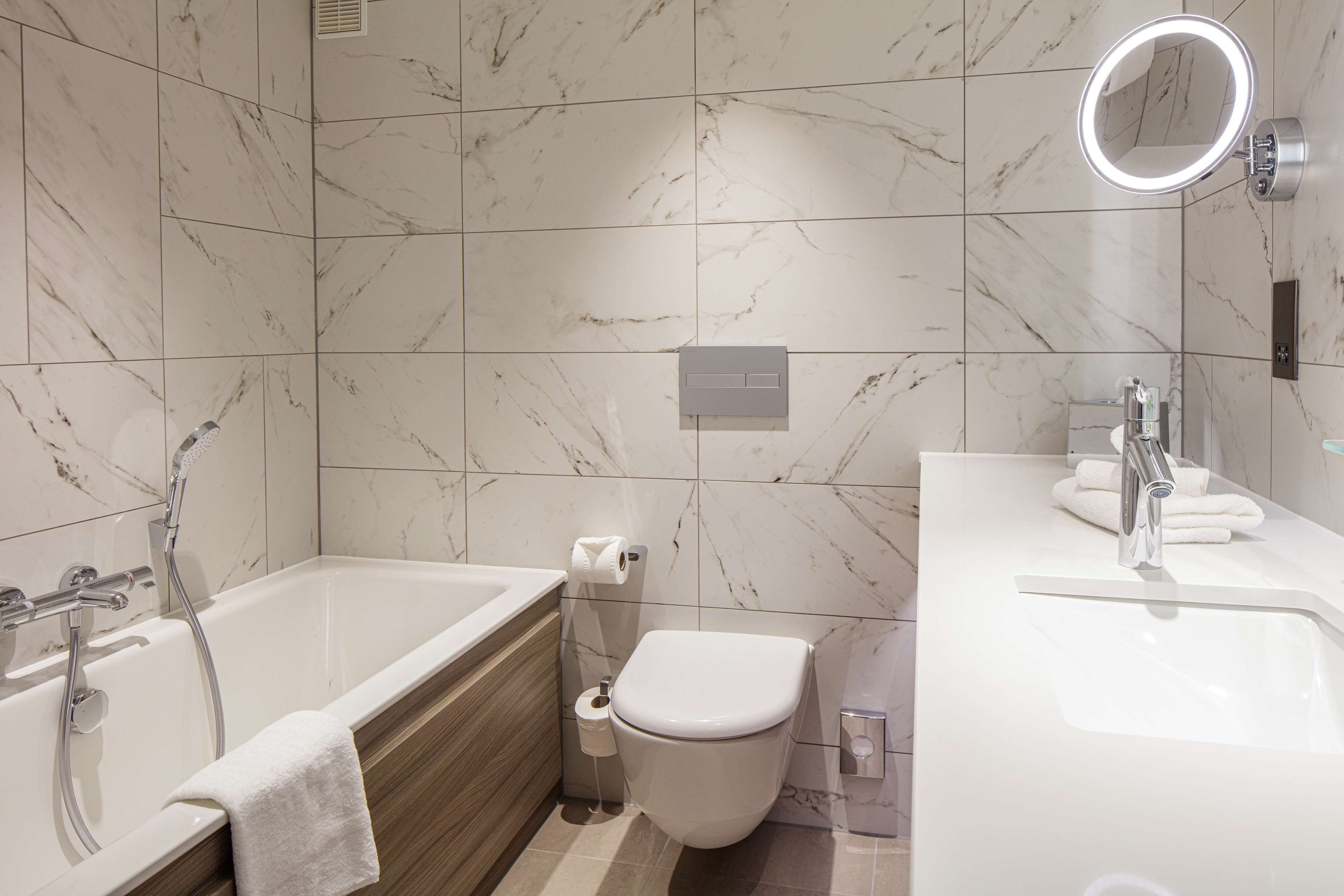 Une salle de bain moderne équipée d’une baignoire, de toilettes et d’un lavabo, le tout recouvert de carreaux de marbre.
