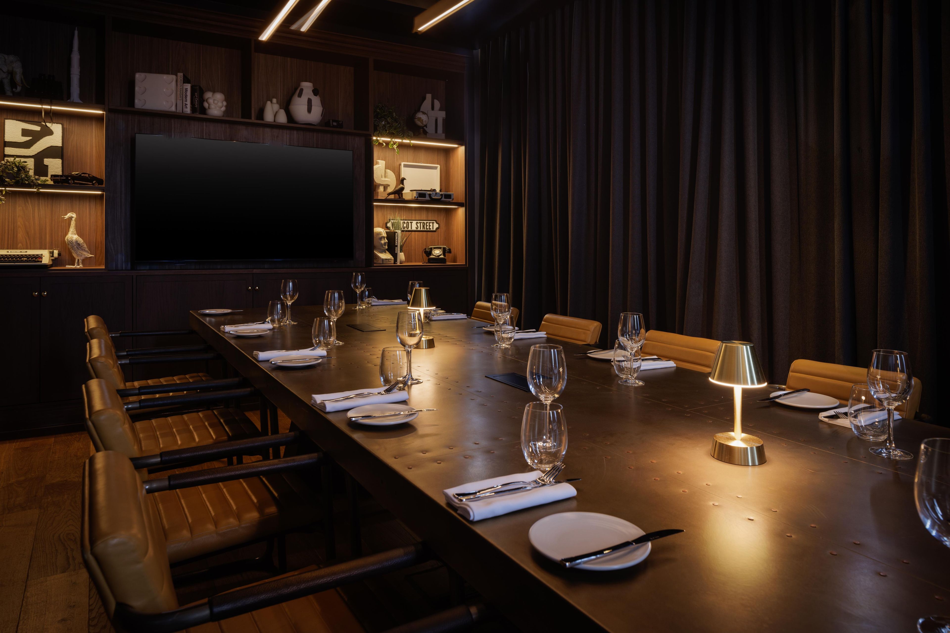 A conference room with a long table set for a meeting, equipped with chairs, plates, cutlery, and wine glasses.
