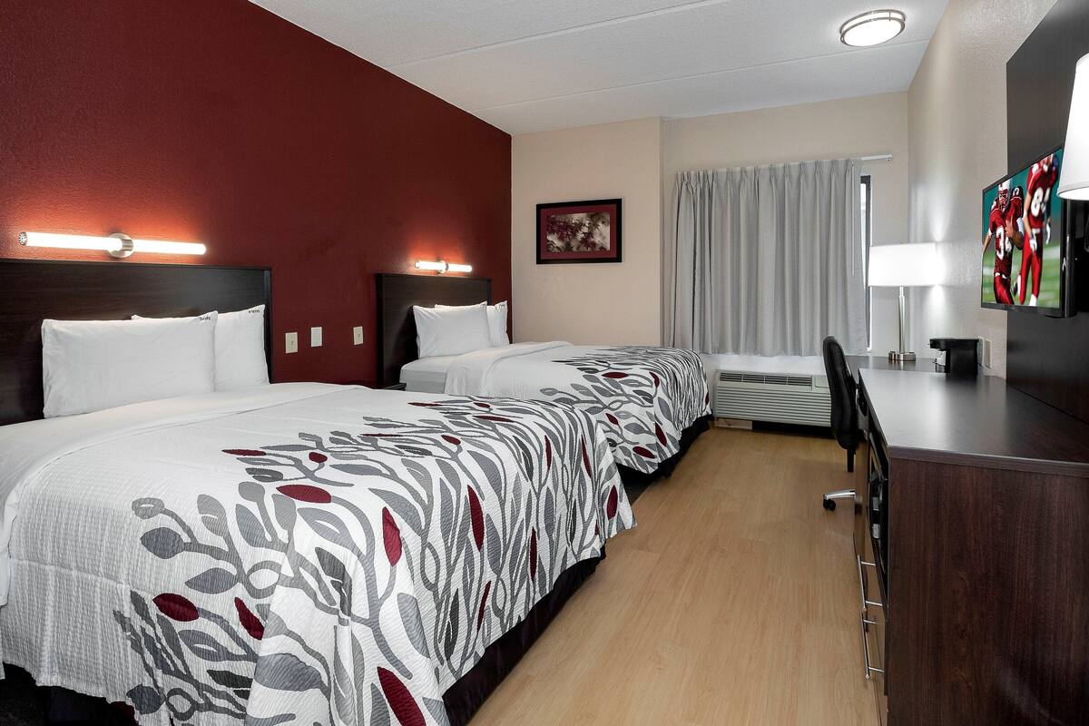 A hotel room with three beds, a desk, a TV, and a window with curtains.