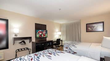 Ein Hotelzimmer mit zwei Betten, einem Fernseher, einem Schreibtisch mit Computer und einem Fenster mit Vorhängen.