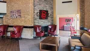 A lobby with brick walls, a Red Roof Inn sign, leather chairs, a wooden coffee table, and a red sofa. - Red Roof Inn Raleigh Southwest - Cary (Cary)