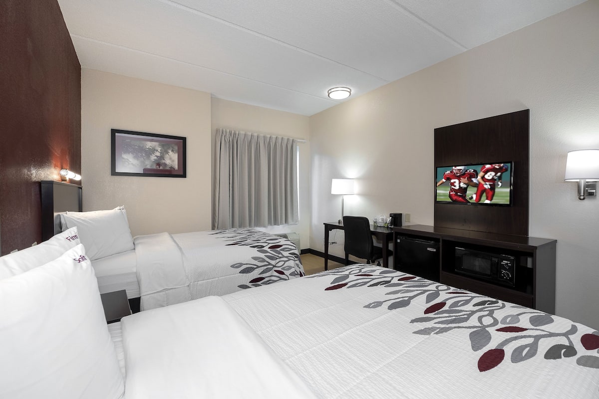 A hotel room with two beds, a desk, a television, and a window with curtains.