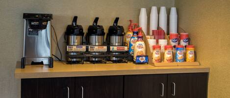 A coffee station with a coffee machine, multiple coffee dispensers, and a selection of coffee creamer bottles.