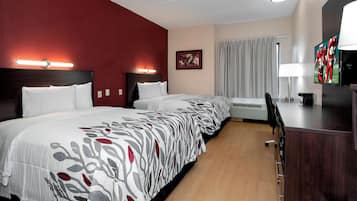 A hotel room with three beds, a desk with a TV, and a window with curtains.