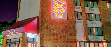 Un hôtel Red Roof Inn reconnaissable à son enseigne au néon bien visible, à sa façade en briques et à son entrée en verre.