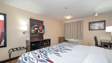 Ein Hotelzimmer mit einem Bett, einem Fernseher, einem Schreibtisch, einem Sessel, einer Mikrowelle und einem Fenster mit Vorhängen.