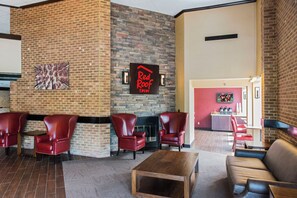 A lobby with brick walls, a Red Roof Inn sign, leather chairs, a wooden coffee table, and a red sofa. - Red Roof Inn Raleigh Southwest - Cary (Cary)