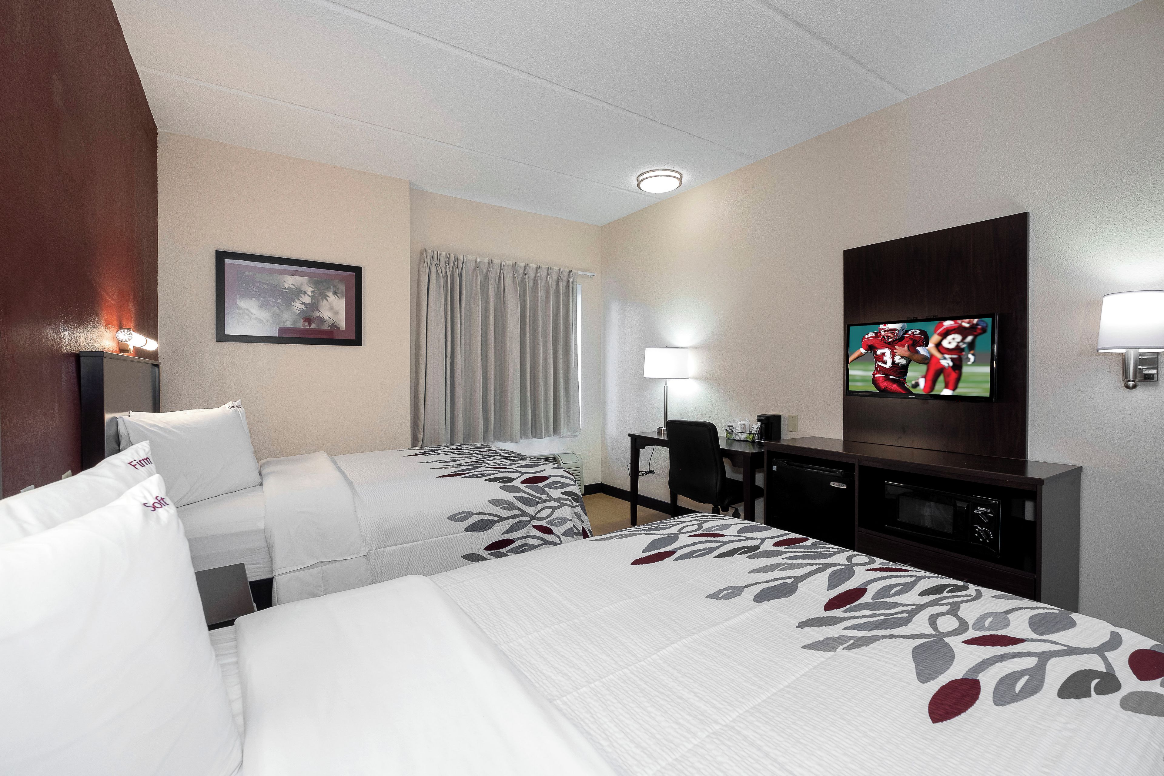 A hotel room with two beds, a desk, a television, and a window with curtains.