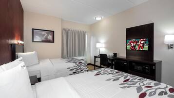 A hotel room with two beds, a desk, a television, and a window with curtains.