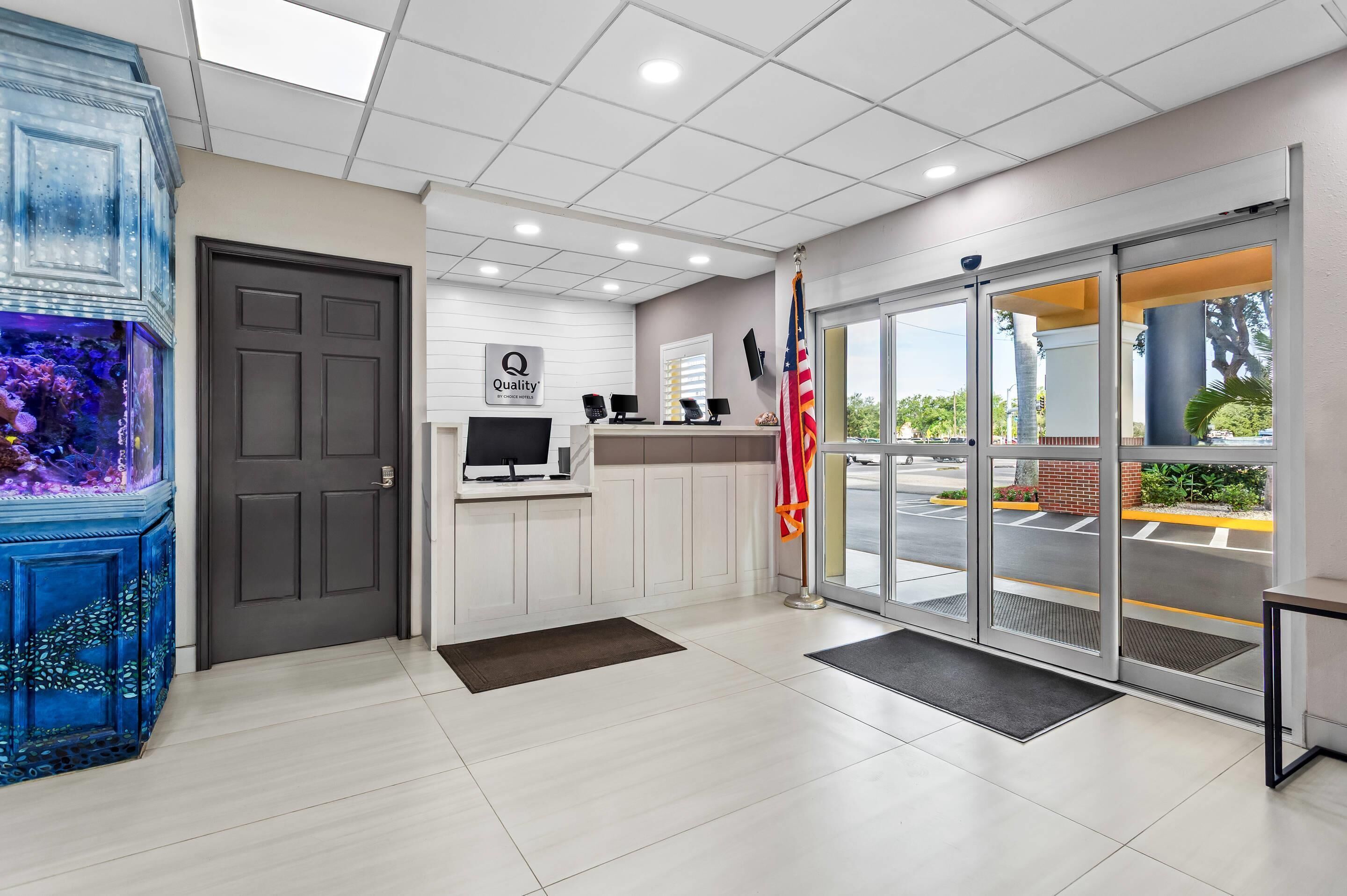 A reception area with a dark door, a sign reading "Quality," two computer monitors, an American flag, and a large aquarium.
