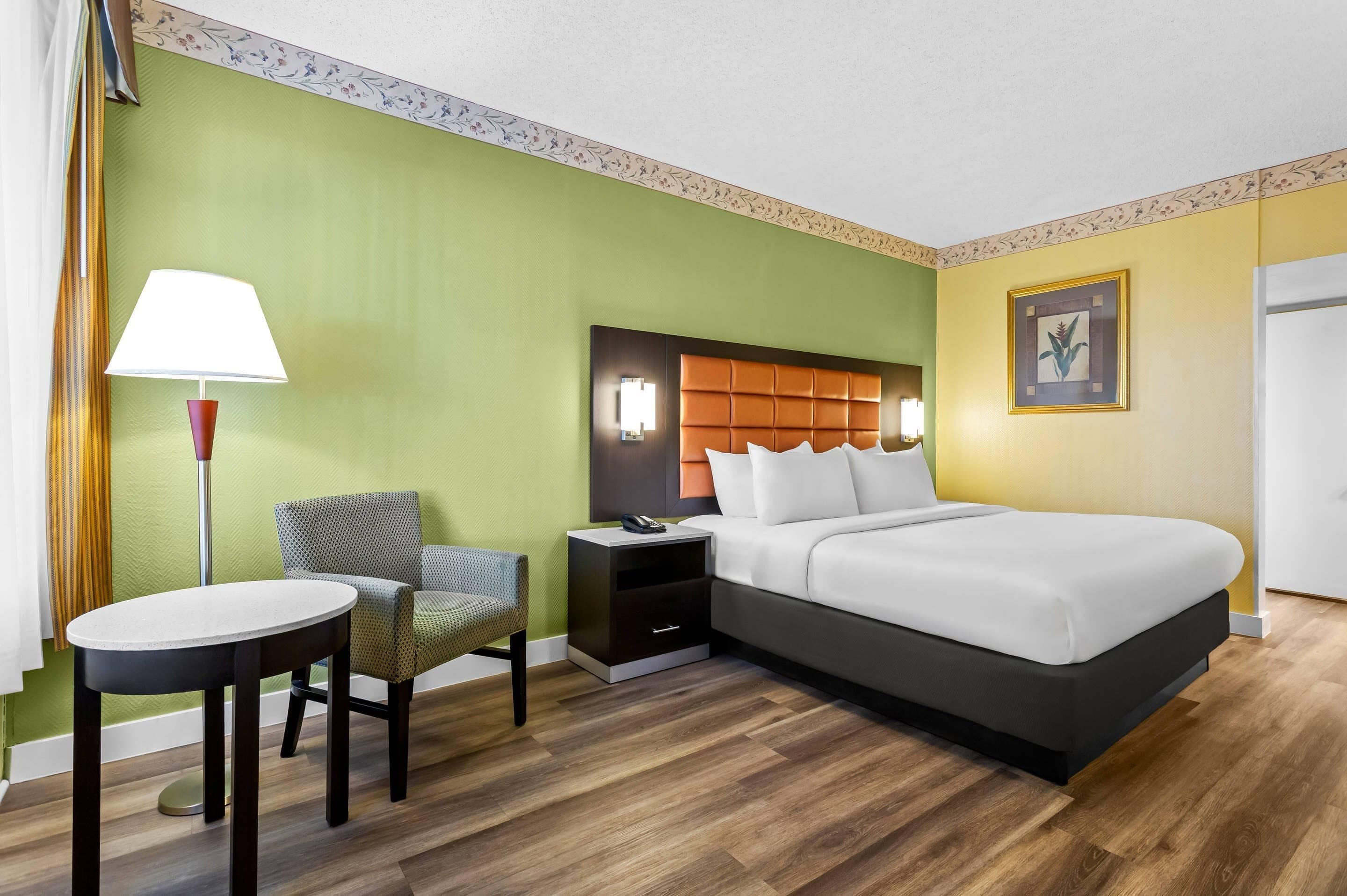 Una camera d'albergo con un letto, un comodino, una sedia, un tavolo e una lampada.