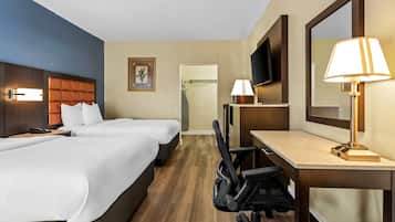 A hotel room with two beds, a desk with a chair, a TV, and a lamp.