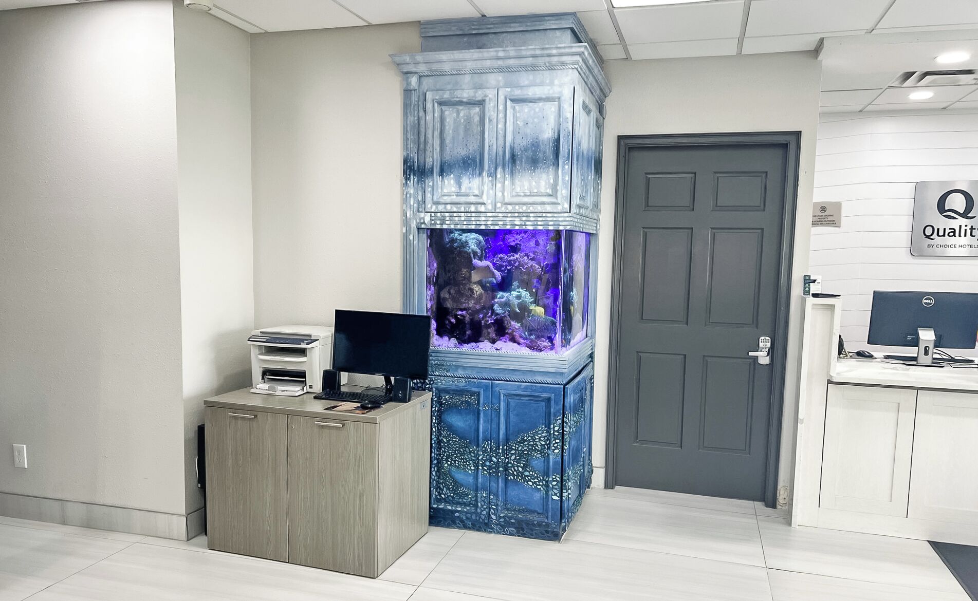 Un mostrador de recepción con una computadora de escritorio, una impresora y un acuario grande.