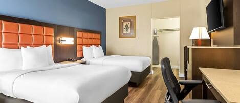A hotel room with two beds, a desk, a chair, a TV, and a lamp.