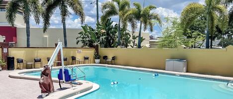 Piscina exterior con trampolín, rodeada de palmeras y sillas.